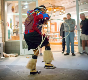 Native American male in fancy regalia hoop dancing in front of a store