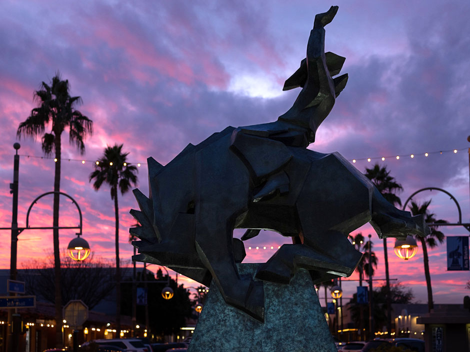 Main Street in Scottsdale Arizona at sunset showing a pink and purple hued sky with a sculpture of a bucking bronco and cowboy silhouetted