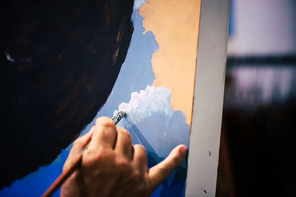 An unseen artist paints cloud or foam-like forms with a small brush in the corner of a canvas over a blue and tan background adjacent to a large black space.